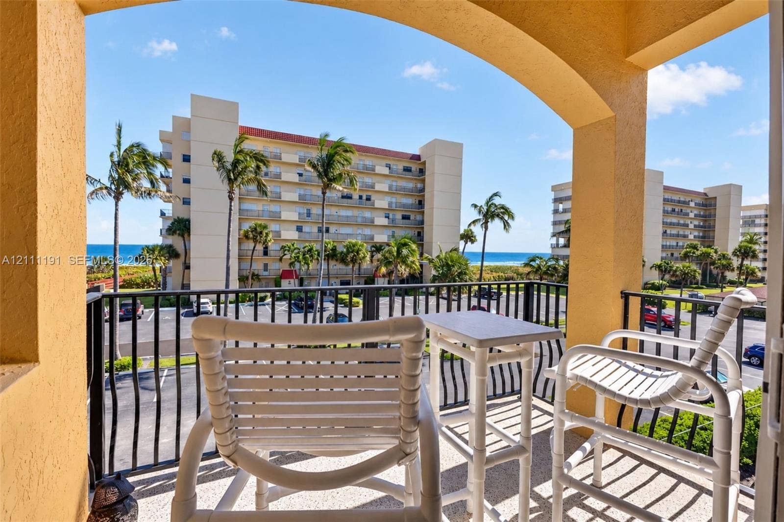 Covered balcony with a textured concrete floor and black metal railing, featuring a coastal backdrop