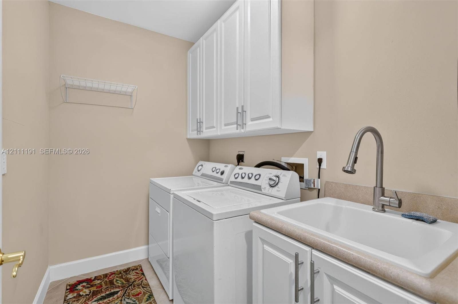 Laundry room featuring white Shaker-style upper cabinetry, a utility sink with a high-arch pull-down faucet, solid surface countertop, and wall-mounted wire shelving