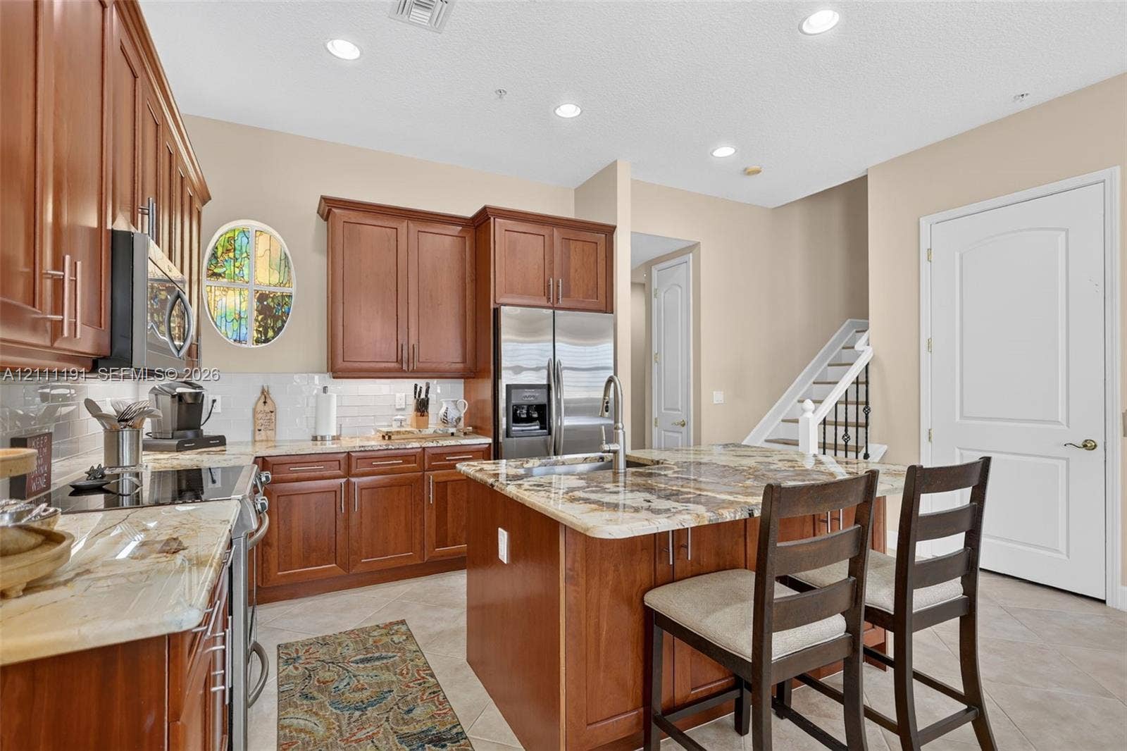 Kitchen featuring wood cabinetry, stone countertops, a center island with a stainless steel sink, tiled backsplash, and recessed lighting