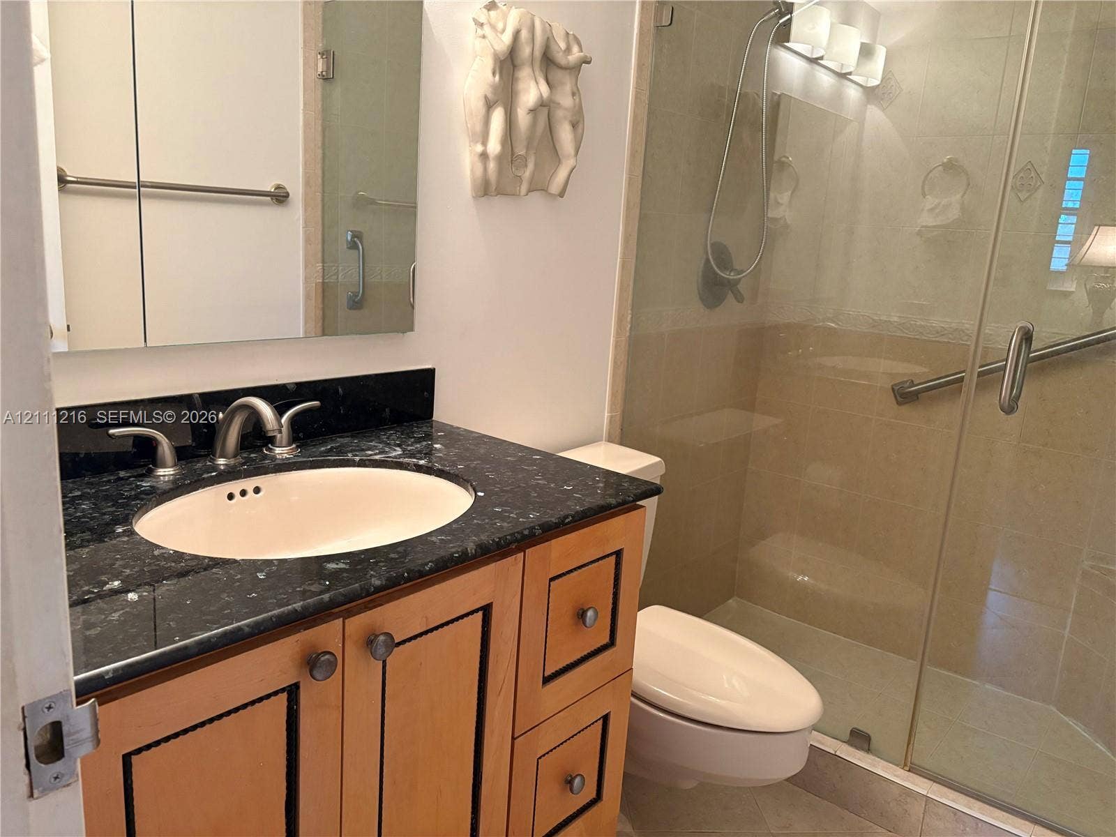 525 Coral Way, #303, Coral Gables, Coral Gables, FL 33134 Wood-finish vanity with a stone countertop, oval undermount sink, glass-enclosed shower, and wall-mounted vanity lighting