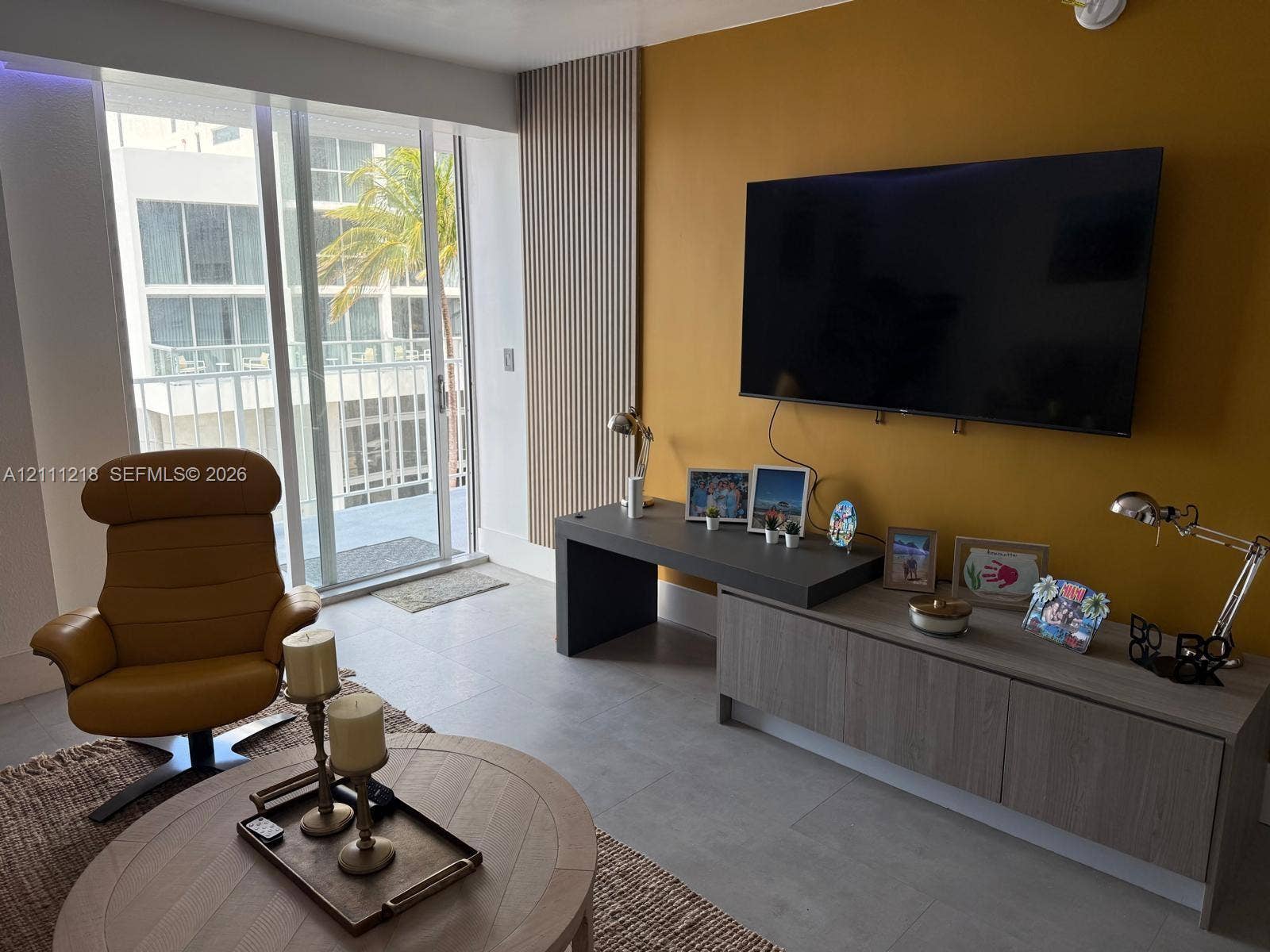 Living area featuring floor-to-ceiling glass sliding doors, accent wall with vertical slat paneling, and large-format tile flooring