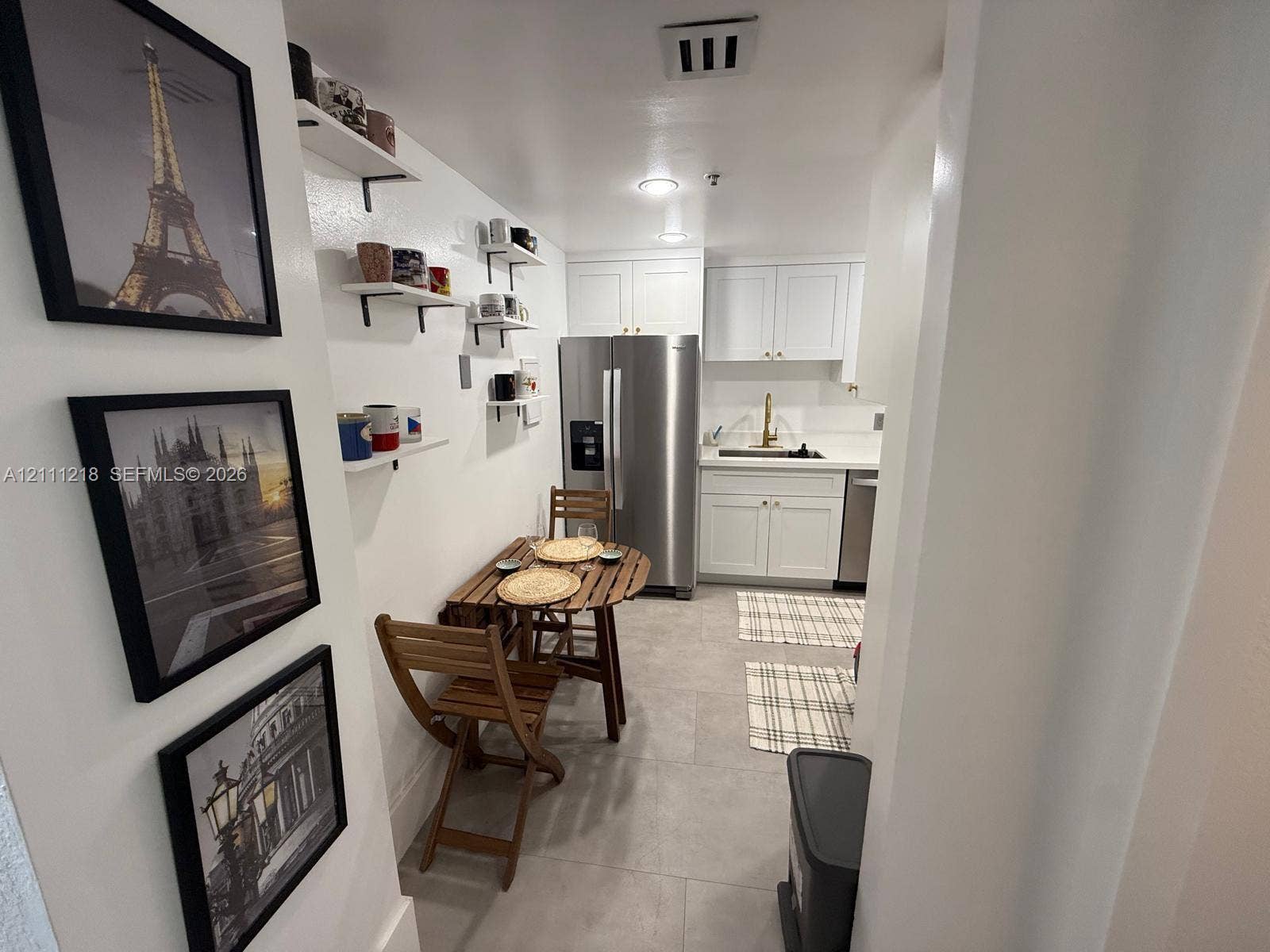 Kitchen featuring white cabinetry, stainless steel refrigerator, stone-composite countertops, built-in wall shelving, and tile flooring