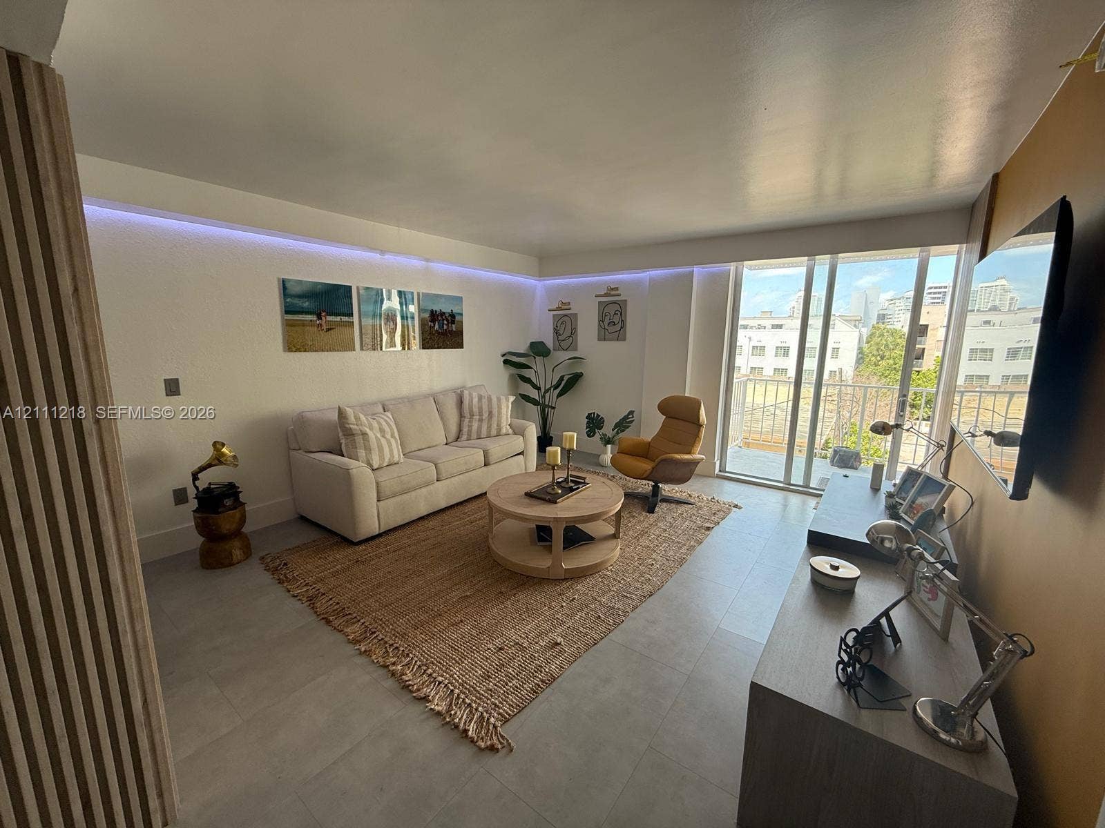 Living area featuring large-format tile flooring, perimeter LED accent lighting, floor-to-ceiling glass sliding doors, and vertical wood-slat wall paneling