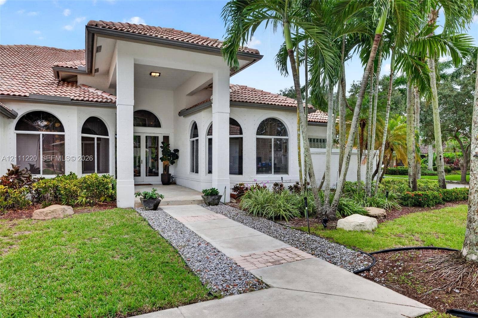 134 Dockside Terrace, Weston, FL 33327 Mediterranean-style exterior featuring a covered entryway, stucco facade, arched windows, concrete walkway, and mature palm trees