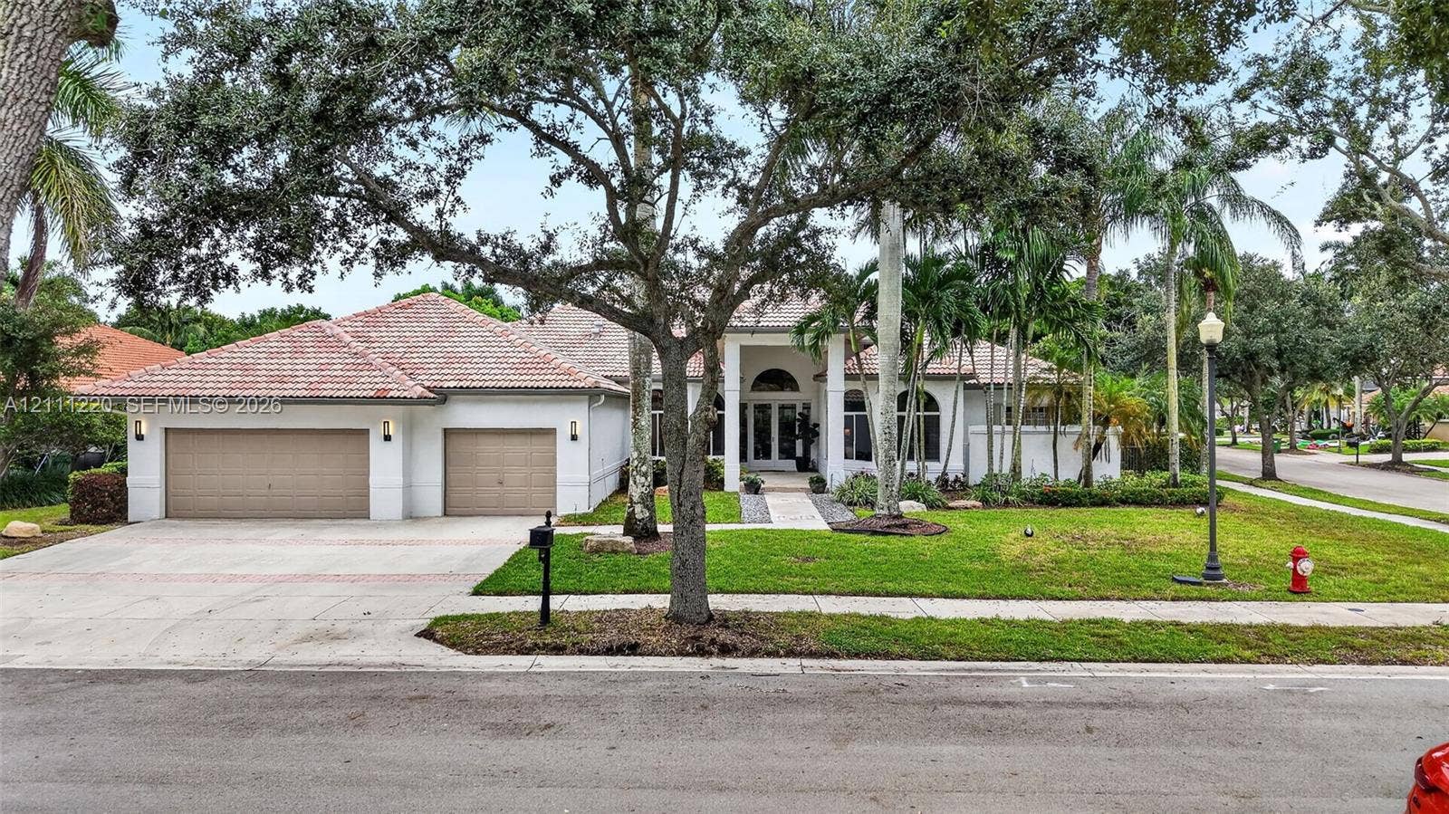 134 Dockside Terrace, Weston, FL 33327 Single-story residence featuring a tile roof, multi-car garage, arched entryway, and mature landscaping