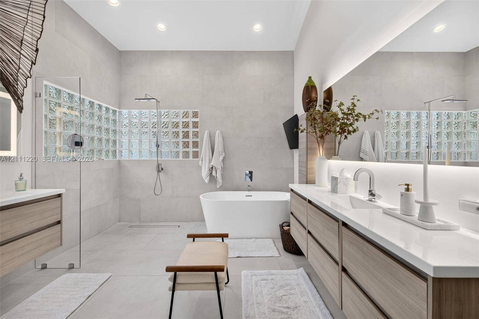 134 Dockside Terrace, Weston, FL 33327 Bathroom featuring a large glass-enclosed shower, freestanding soaking tub, dual-sink vanity with light wood-finish cabinetry, quartz countertops, and back-lit wall mirror