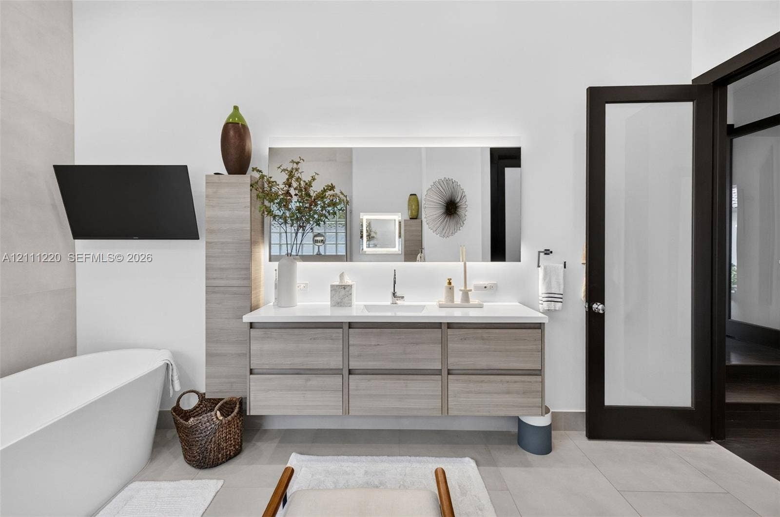 134 Dockside Terrace, Weston, FL 33327 Floating wood-finish vanity with an integrated countertop, rectangular undermount sink, backlit rectangular mirror, and a freestanding soaking tub