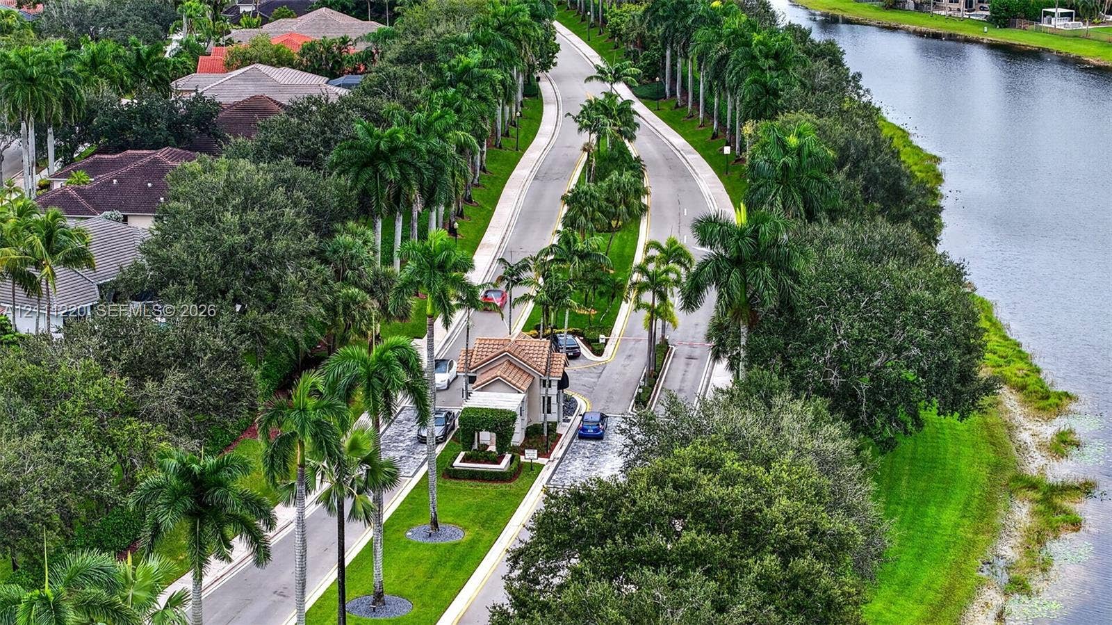134 Dockside Terrace, Weston, FL 33327 Gated entrance featuring a tile-roof structure, bordered by palm-lined streets, mature landscaping, and an expansive waterway