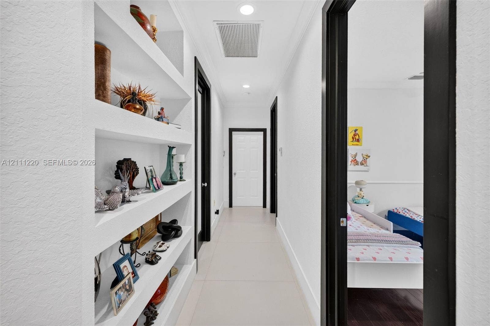 134 Dockside Terrace, Weston, FL 33327 Hallway featuring built-in recessed wall shelving, high-contrast dark door casings, smooth wall finish, and neutral tile flooring