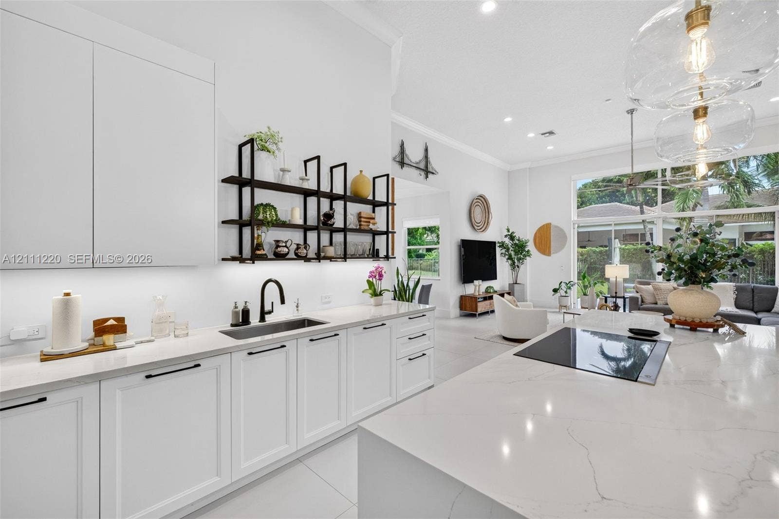 134 Dockside Terrace, Weston, FL 33327 Kitchen featuring white shaker-style cabinetry, a large central island with a solid surface countertop, matte black hardware, under-cabinet lighting, and built-in glass pendant illumination