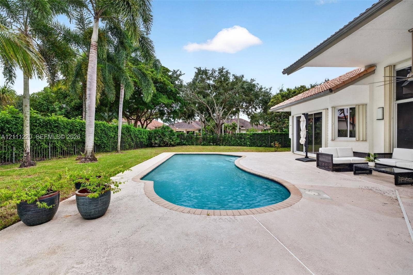 134 Dockside Terrace, Weston, FL 33327 Backyard featuring an in-ground swimming pool, concrete patio, perimeter hedges, and palm trees