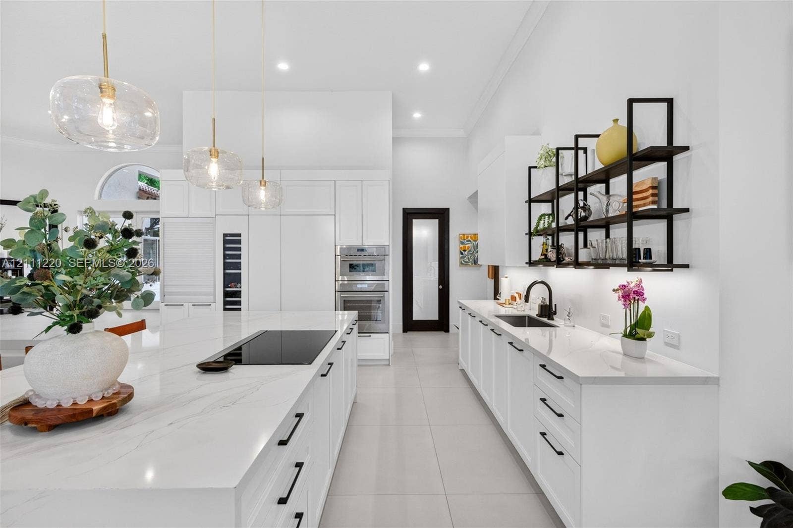 134 Dockside Terrace, Weston, FL 33327 Modern kitchen featuring a stone-surface island with an integrated induction cooktop, white cabinetry with matte black hardware, stainless steel double wall ovens, glass pendant lighting, and black metal open shelving