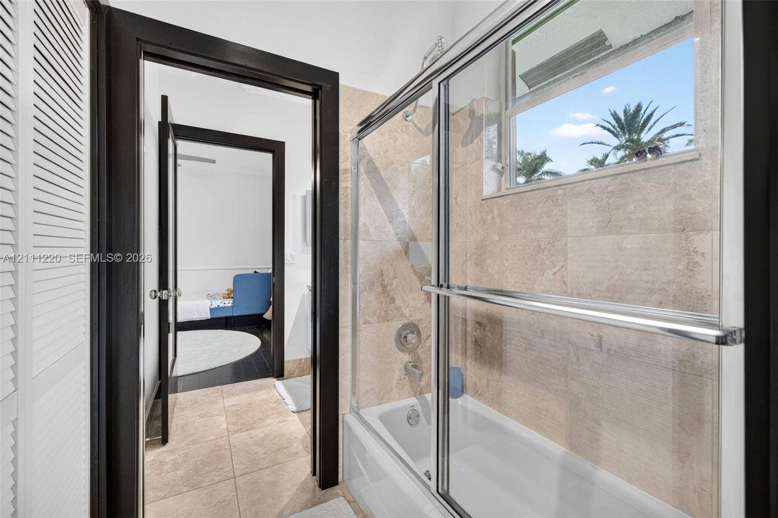 134 Dockside Terrace, Weston, FL 33327 Full bathroom featuring a tub-shower combination with a sliding glass enclosure, large-format stone-finish wall and floor tiling, and dark-finished door trim