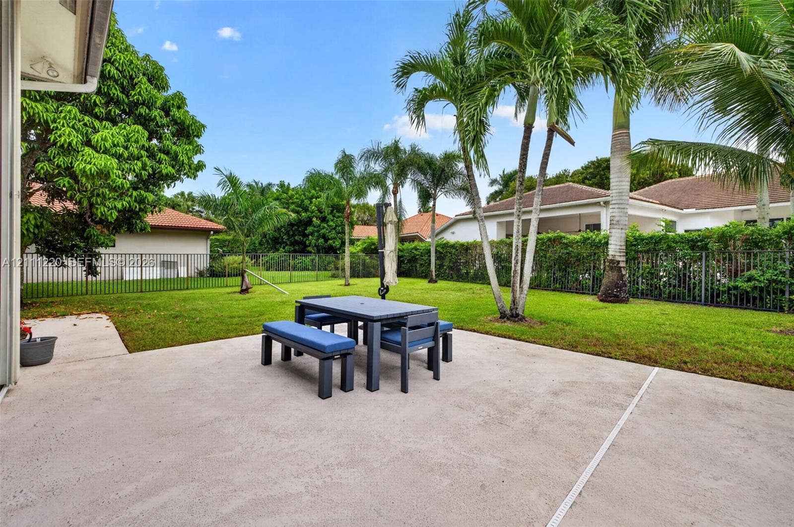 134 Dockside Terrace, Weston, FL 33327 Concrete patio featuring a sodded lawn, perimeter metal fencing, and mature palm trees