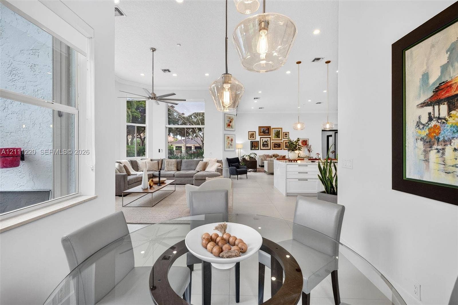 134 Dockside Terrace, Weston, FL 33327 Open-concept interior featuring large-format tile flooring, recessed lighting, expansive windows, and tiered glass pendant fixtures over the dining area