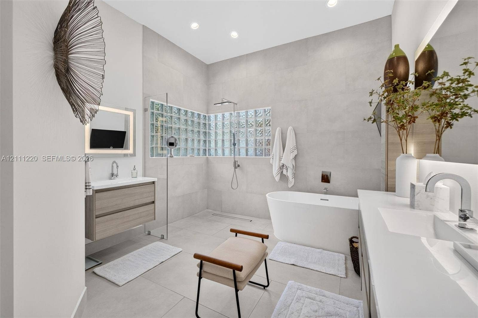 134 Dockside Terrace, Weston, FL 33327 Bathroom featuring a freestanding soaking tub, glass-enclosed shower with glass block accent wall, wall-mounted wood-finish vanity, and integrated LED-lit vanity mirror