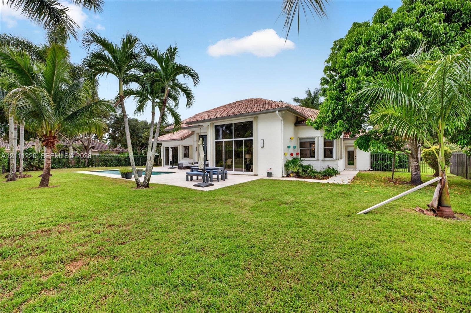 134 Dockside Terrace, Weston, FL 33327 Expansive backyard featuring a concrete patio, swimming pool, mature palm trees, and floor-to-ceiling glass windows