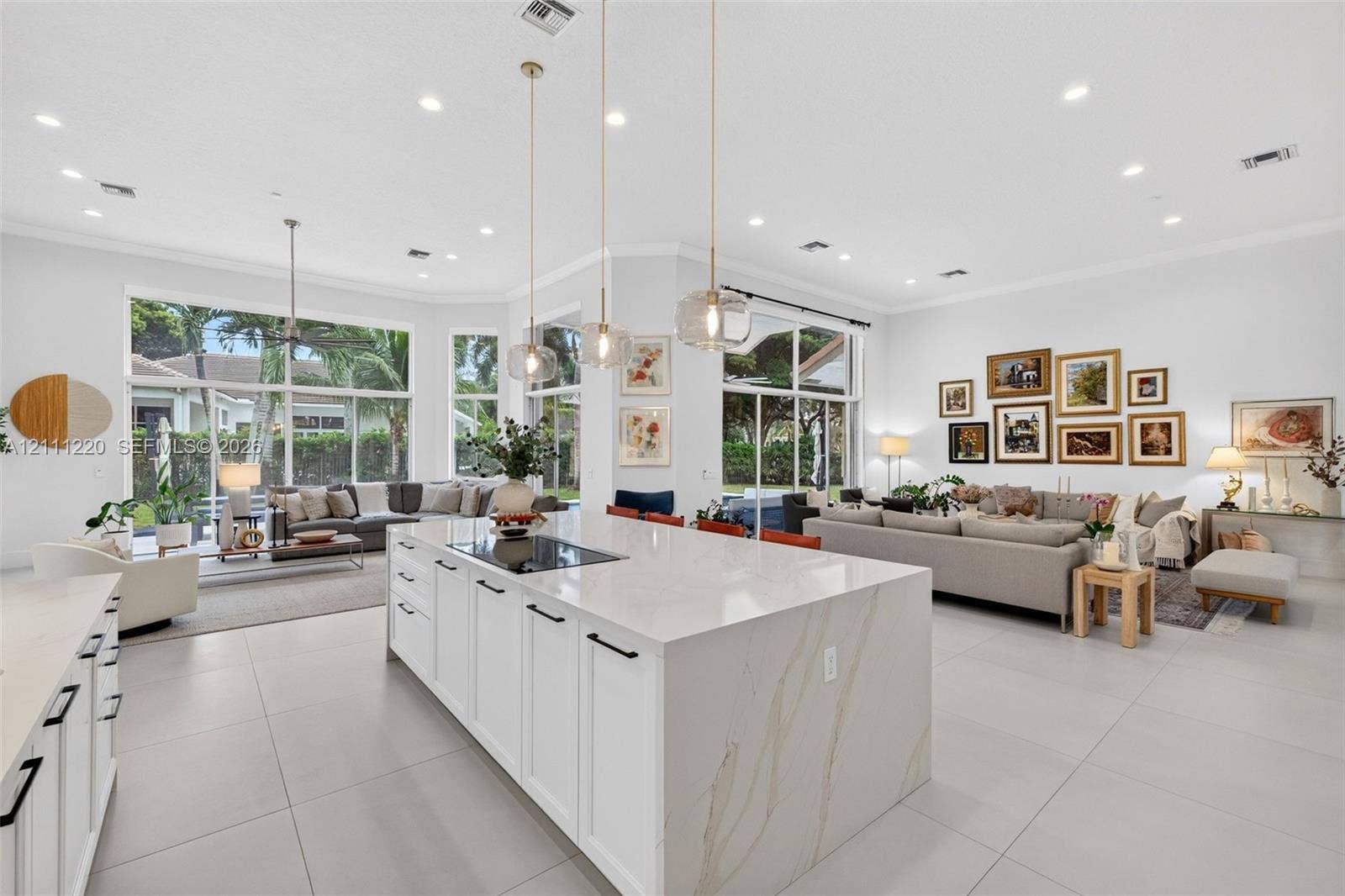 134 Dockside Terrace, Weston, FL 33327 Large kitchen island with a stone-finish waterfall countertop, integrated cooktop, white shaker-style cabinetry, matte black hardware, and three glass pendant lights