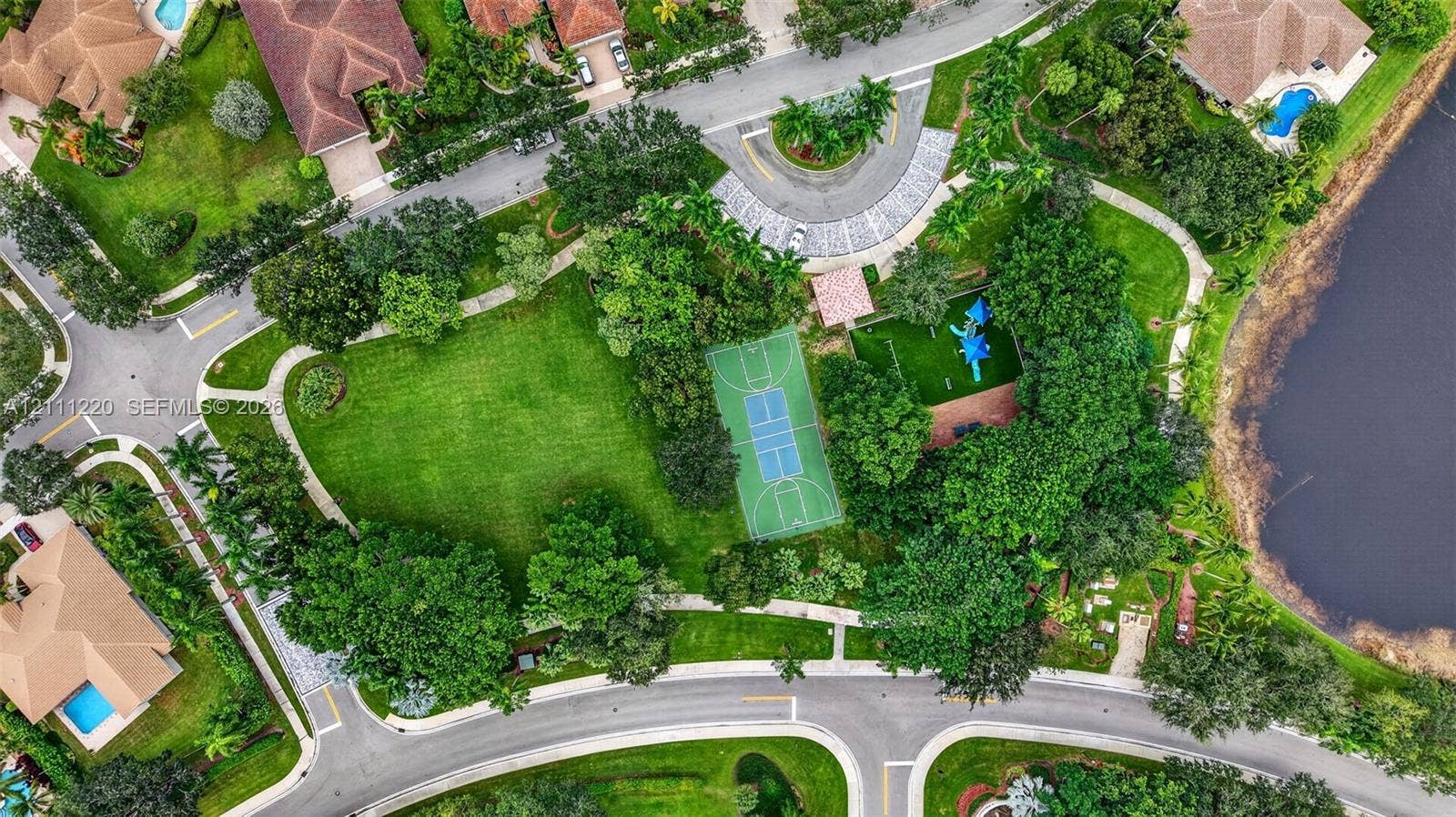 134 Dockside Terrace, Weston, FL 33327 Aerial perspective of a community recreation area featuring a basketball court, playground, expansive green space, mature trees, and a bordering water feature