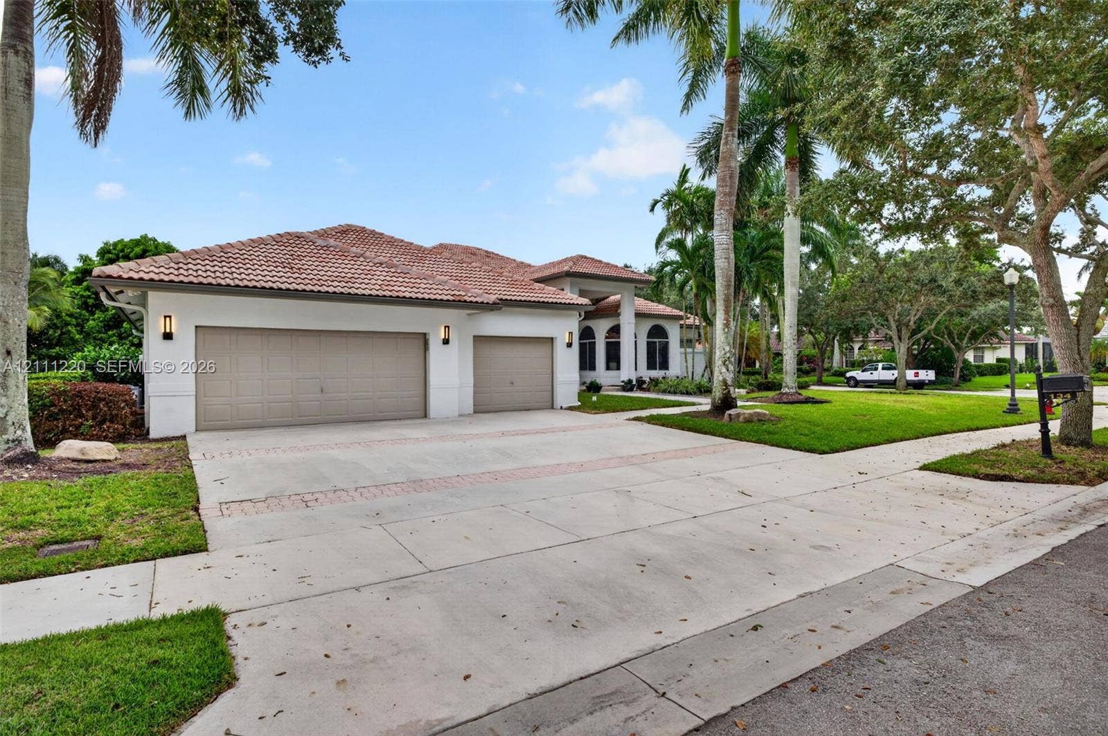 134 Dockside Terrace, Weston, FL 33327 Stucco exterior featuring a multi-gable tile roof, three-car garage, concrete driveway with brick inlay, and mature landscaping