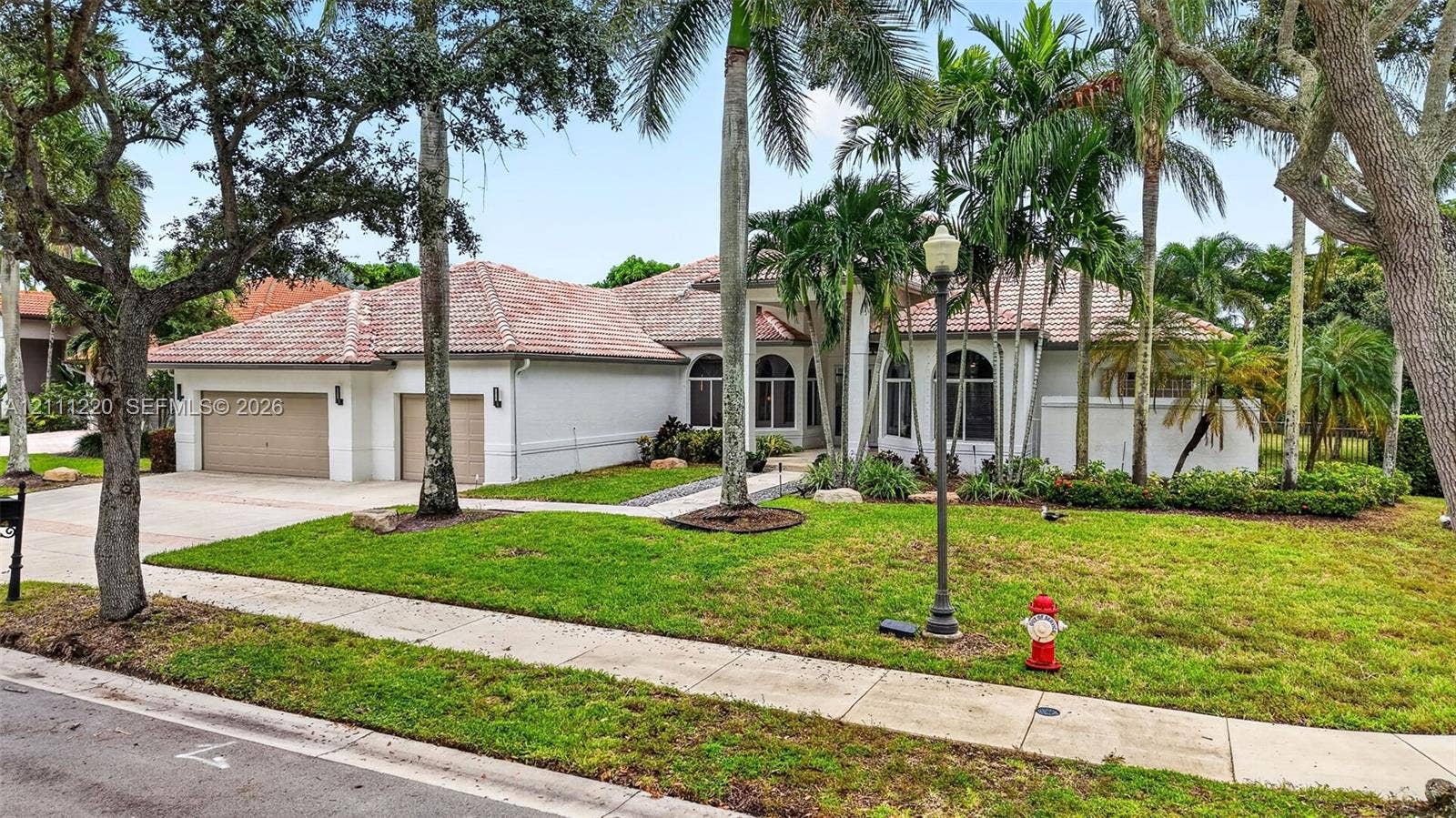 134 Dockside Terrace, Weston, FL 33327 Single-story stucco exterior featuring a multi-car garage, arched windows, and a tiled roof, set within a landscaped lot with mature palm trees