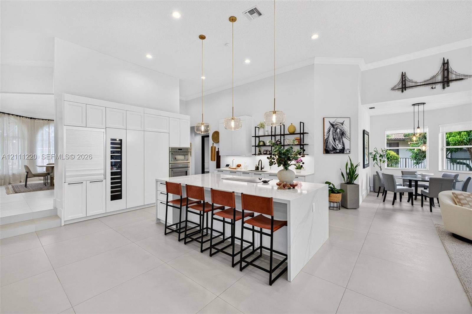 134 Dockside Terrace, Weston, FL 33327 Gourmet kitchen featuring a large central island with stone-finish countertops, custom floor-to-ceiling white cabinetry, integrated stainless steel appliances, tiered pendant lighting, and oversized neutral tile flooring