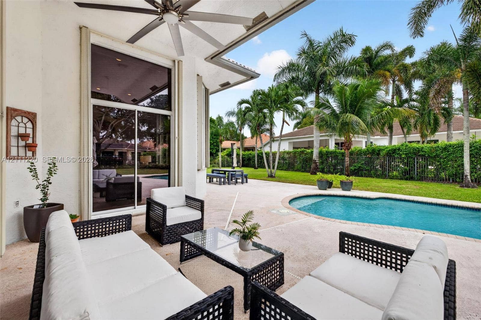 134 Dockside Terrace, Weston, FL 33327 Covered patio featuring a ceiling fan, sliding glass doors, concrete decking, and a swimming pool set within a fenced yard with mature palms