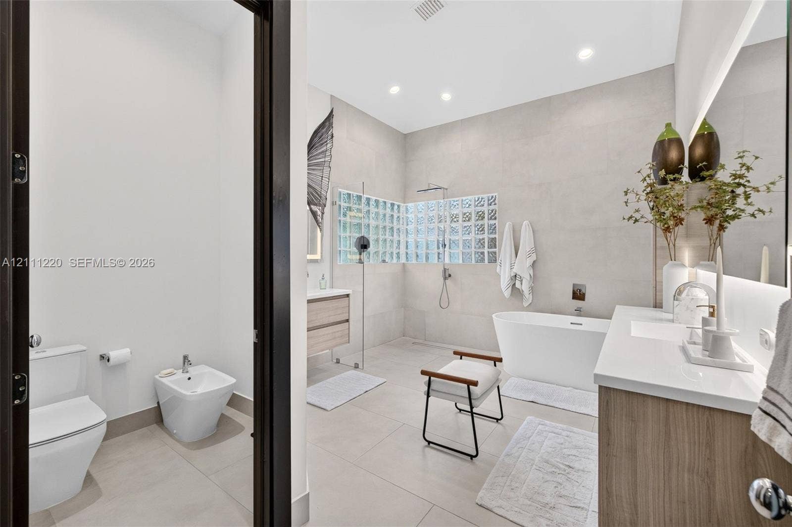 134 Dockside Terrace, Weston, FL 33327 Bathroom featuring a large freestanding soaking tub, walk-in shower with glass block accent wall, double vanity with wood-finish cabinetry, wall-mounted faucet fixtures, and ceramic tile flooring