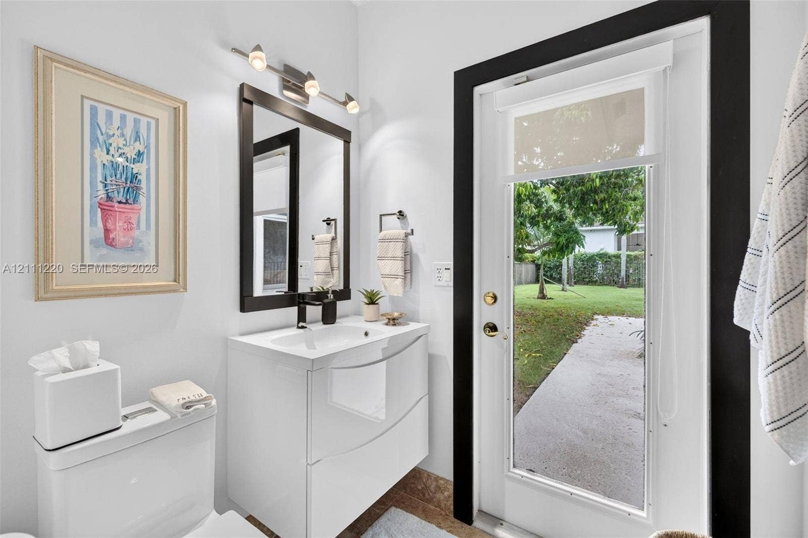 134 Dockside Terrace, Weston, FL 33327 Modern floating vanity with a vessel sink, dark-framed vanity mirror, multi-bulb wall-mounted lighting, and an exterior glass door leading to a concrete walkway