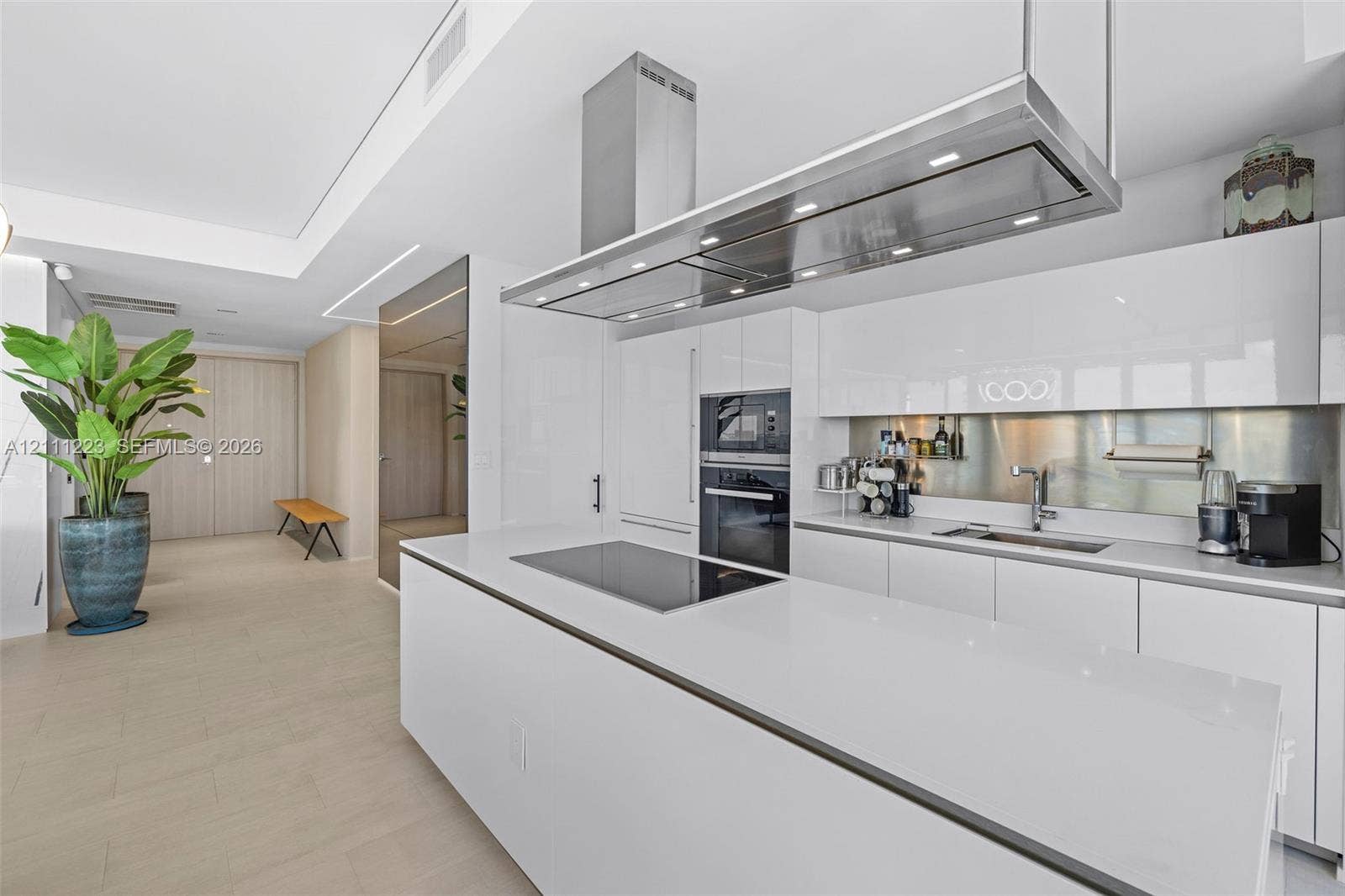 Kitchen featuring high-gloss cabinetry, a spacious island with an integrated induction cooktop, a stainless steel range hood, and a metallic backsplash