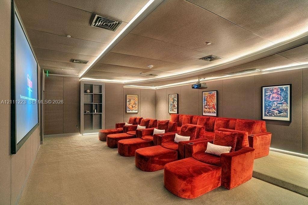 Media room featuring a wall-mounted projector screen, built-in recessed shelving, integrated perimeter LED accent lighting, and tiered flooring