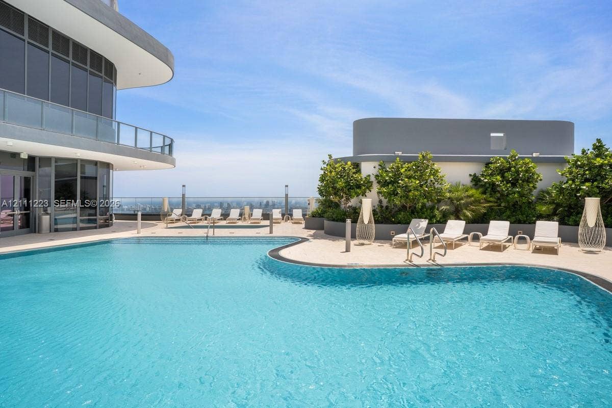 Rooftop terrace featuring a curved swimming pool, stone-finish pool deck, glass railing, and integrated landscaping