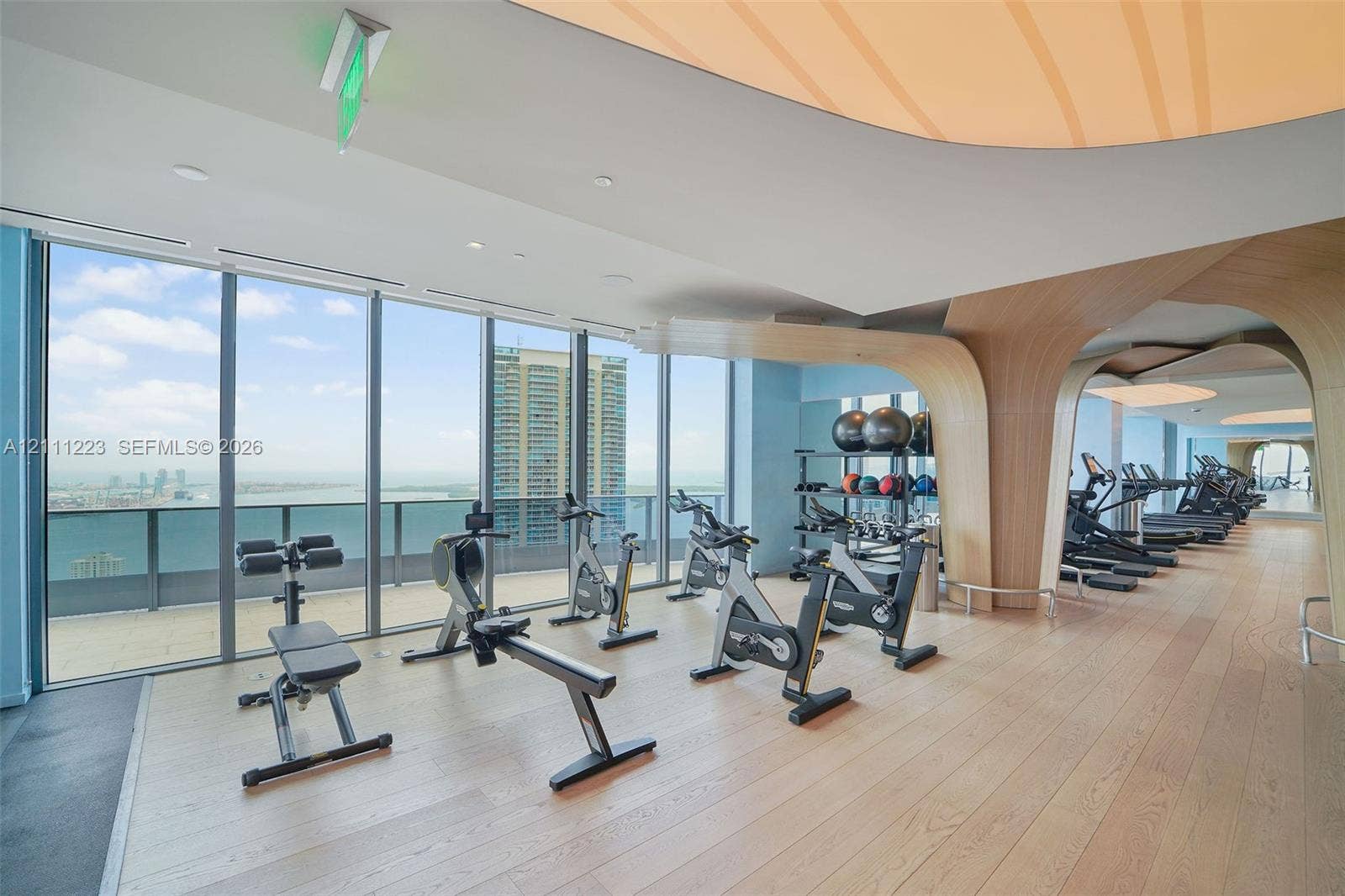 Fitness center featuring floor-to-ceiling windows, wood-finish flooring, sculptural wood-veneer architectural accents, and recessed cove lighting