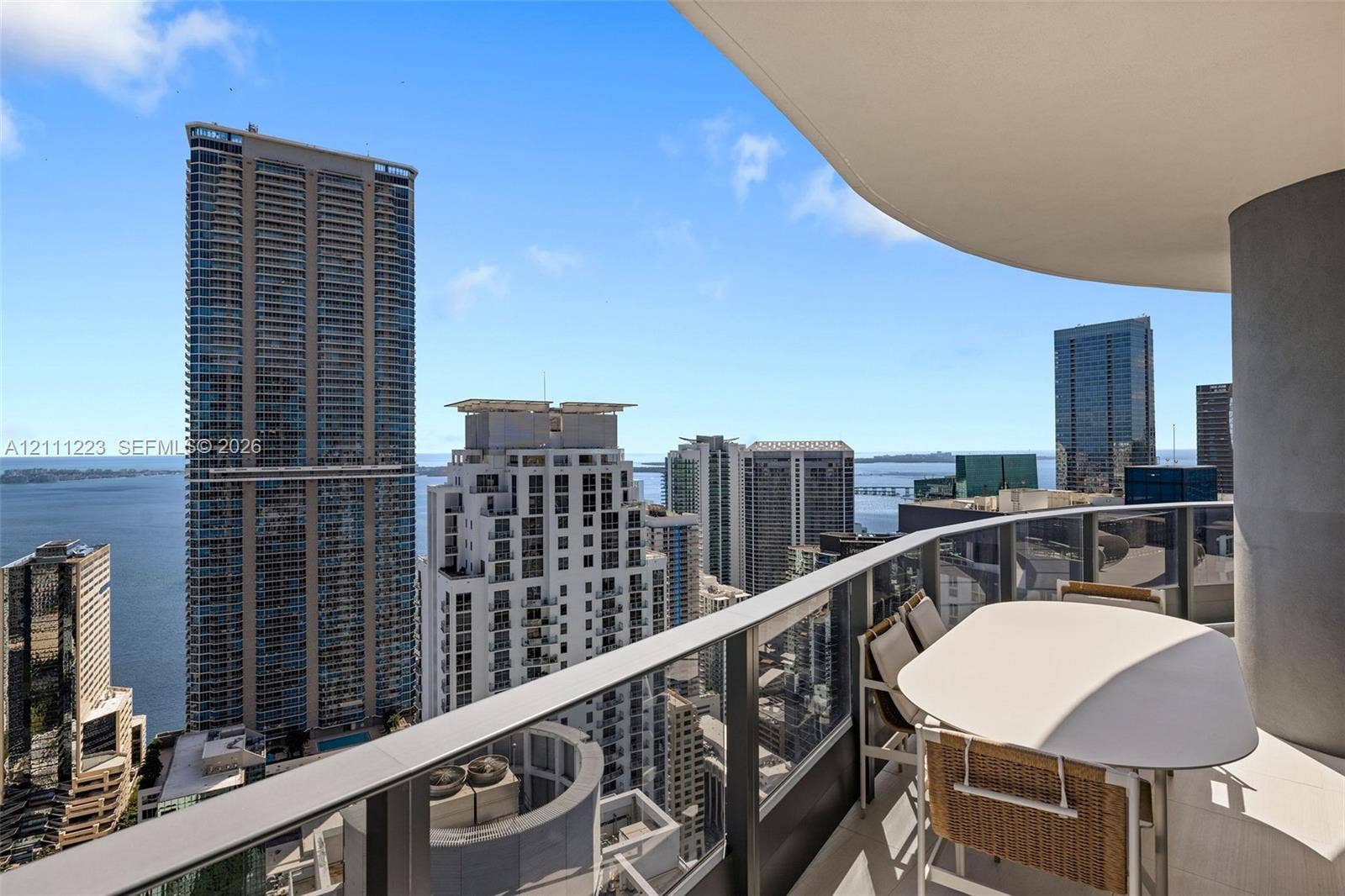 Curved private balcony with glass railing, concrete overhead covering, and panoramic urban and water scenery