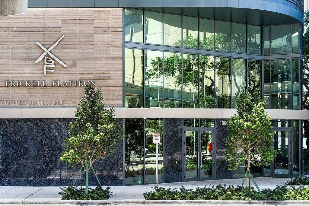 Contemporary high-rise facade featuring floor-to-ceiling glass paneling, stone tile exterior cladding, polished dark stone accents, and integrated entryway glass doors