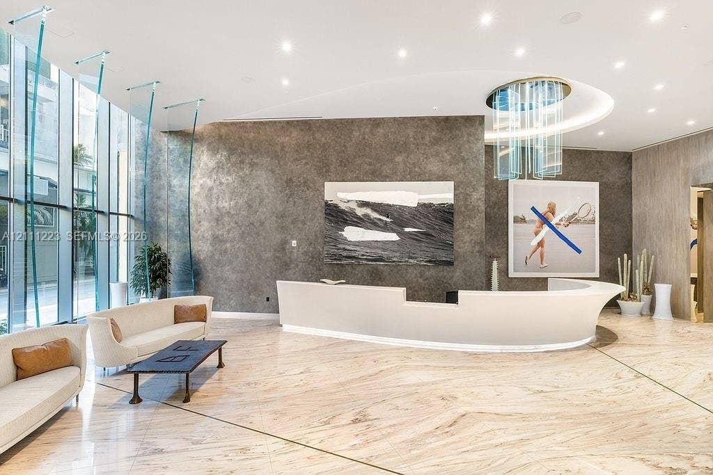 Lobby featuring floor-to-ceiling glass windows, stone flooring, textured wall finishes, a curved built-in reception desk, and a tiered glass chandelier
