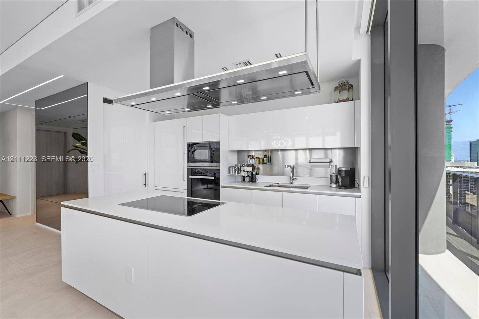 Kitchen featuring white gloss cabinetry, expansive island with integrated cooktop, stainless steel range hood, built-in wall oven, and metallic backsplash