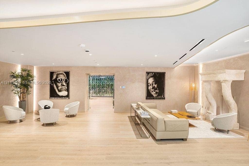 Spacious interior featuring light-toned wood-finish flooring, recessed ceiling lighting with perimeter cove detailing, and a sculptural stone fireplace surround