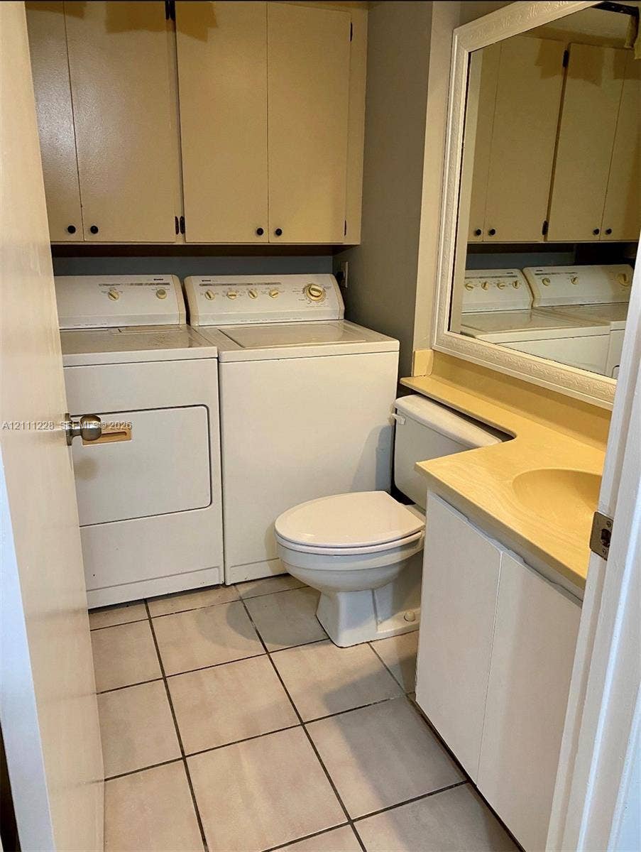 Laundry area featuring upper storage cabinetry, tile flooring, a vanity with a solid-surface countertop, and a wall-mounted mirror