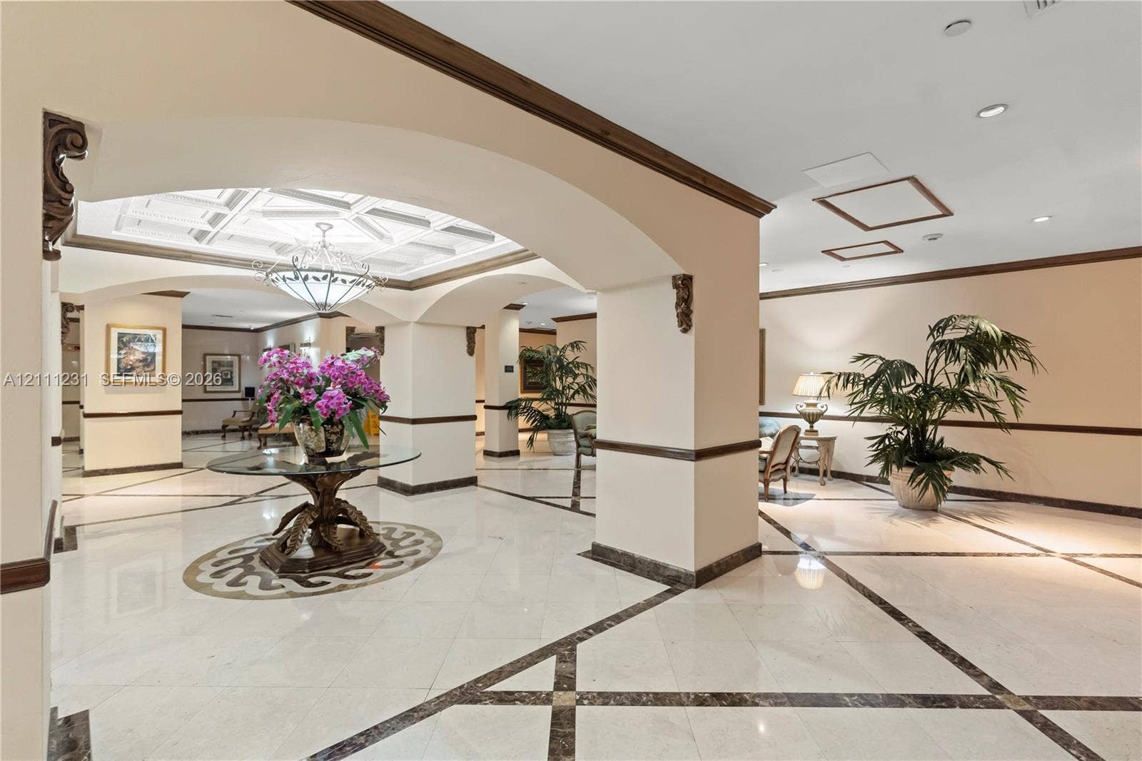 Grand foyer featuring large-format tile flooring with decorative stone inlays, coffered ceilings, structural arched openings, and custom millwork detailing