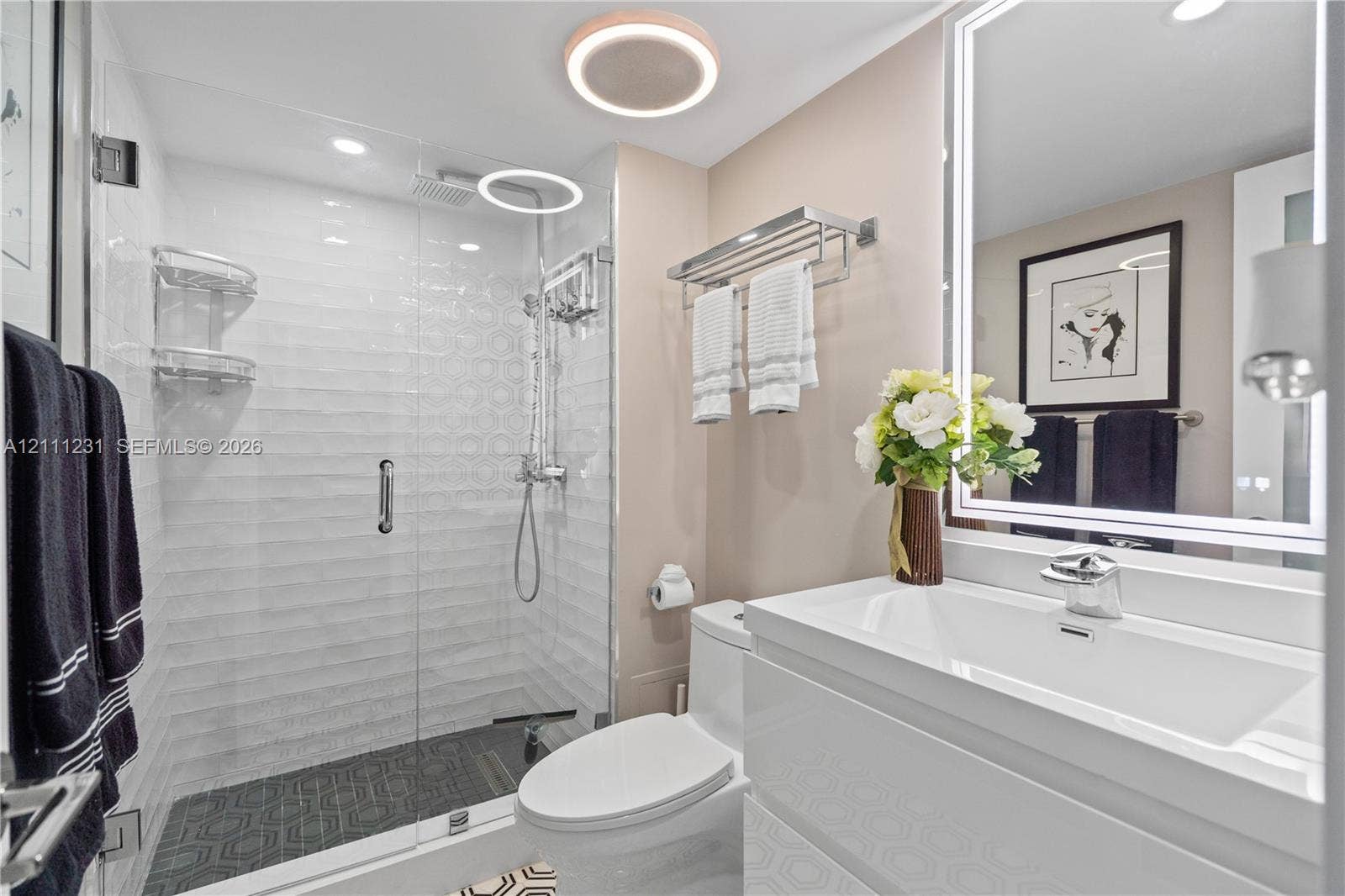 Walk-in shower with a glass enclosure, textured wall tile, and geometric floor tile; wall-mounted vanity with an integrated basin; LED-backlit vanity mirror; and contemporary flush-mount ceiling lighting