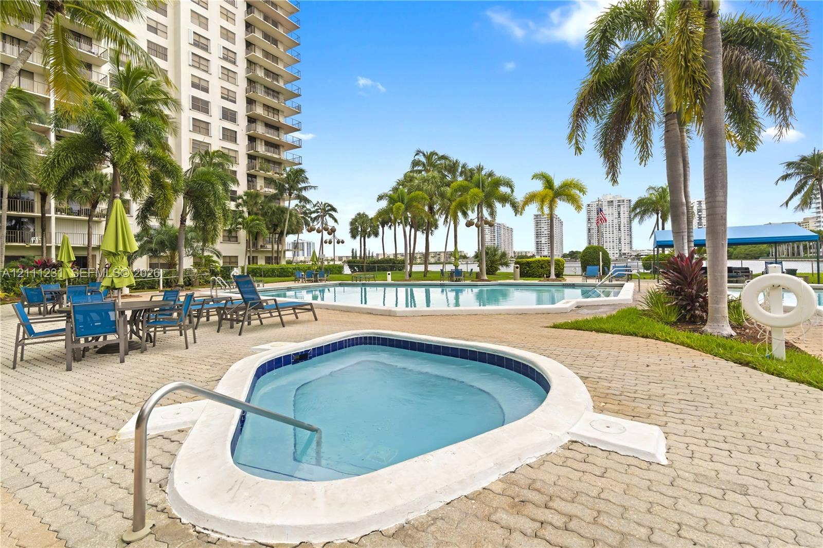 Outdoor pool and spa area featuring a paver deck, palm trees, and waterfront perimeter