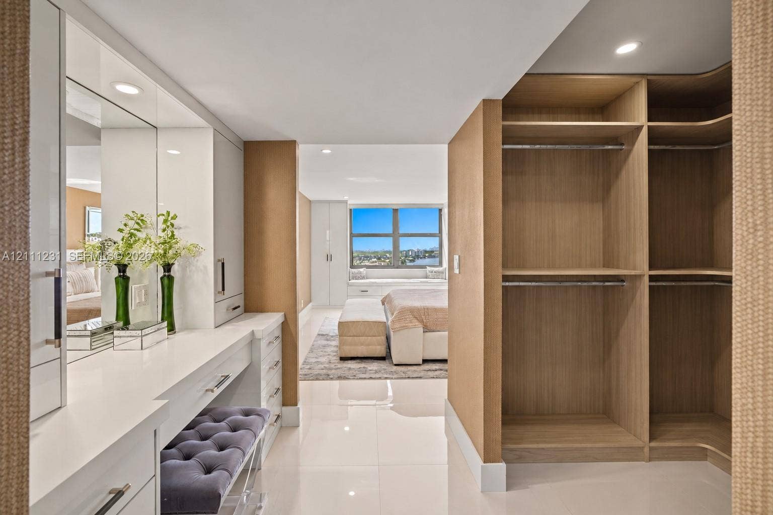 Custom built-in vanity featuring white high-gloss cabinetry, countertop, and integrated mirror, paired with open-shelf wood-finish wardrobe storage and polished large-format flooring