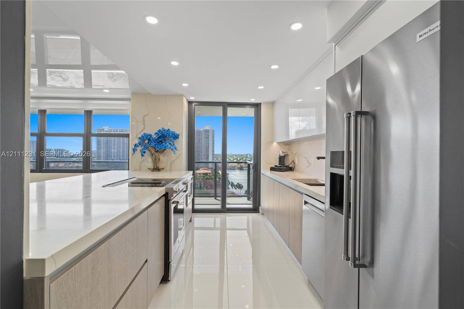 Modern kitchen featuring flat-panel cabinetry, light-toned stone countertops, integrated stainless steel appliances, recessed ceiling lighting, and polished large-format tile flooring