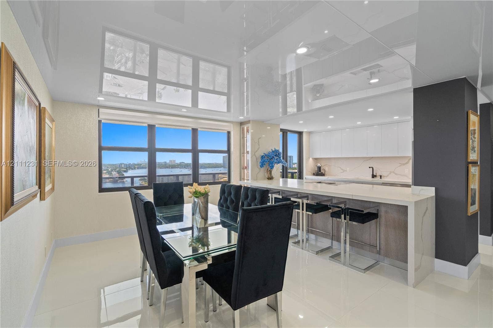 High-gloss ceiling with recessed lighting, expansive windows featuring water scenery, kitchen island with quartz-style countertop, slab backsplash, and flat-panel cabinetry