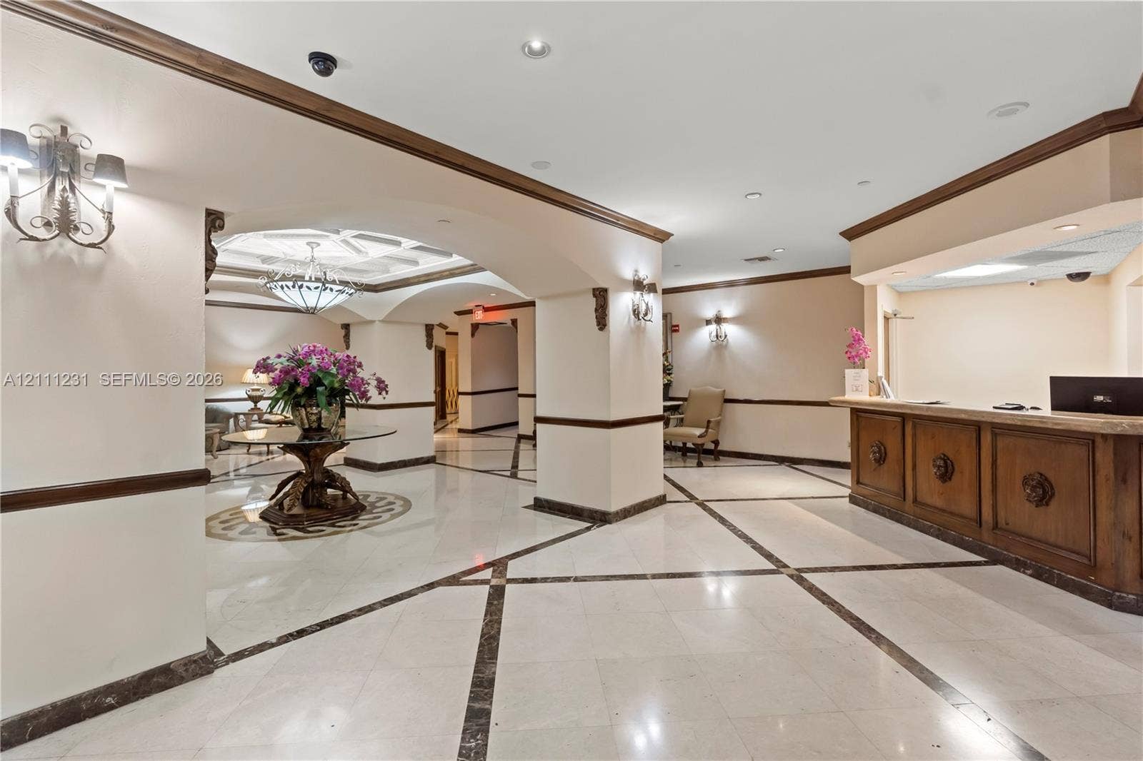 Lobby featuring arched architectural details, stone tile flooring with decorative inlay, built-in wooden reception desk, recessed lighting, and wall-mounted sconces