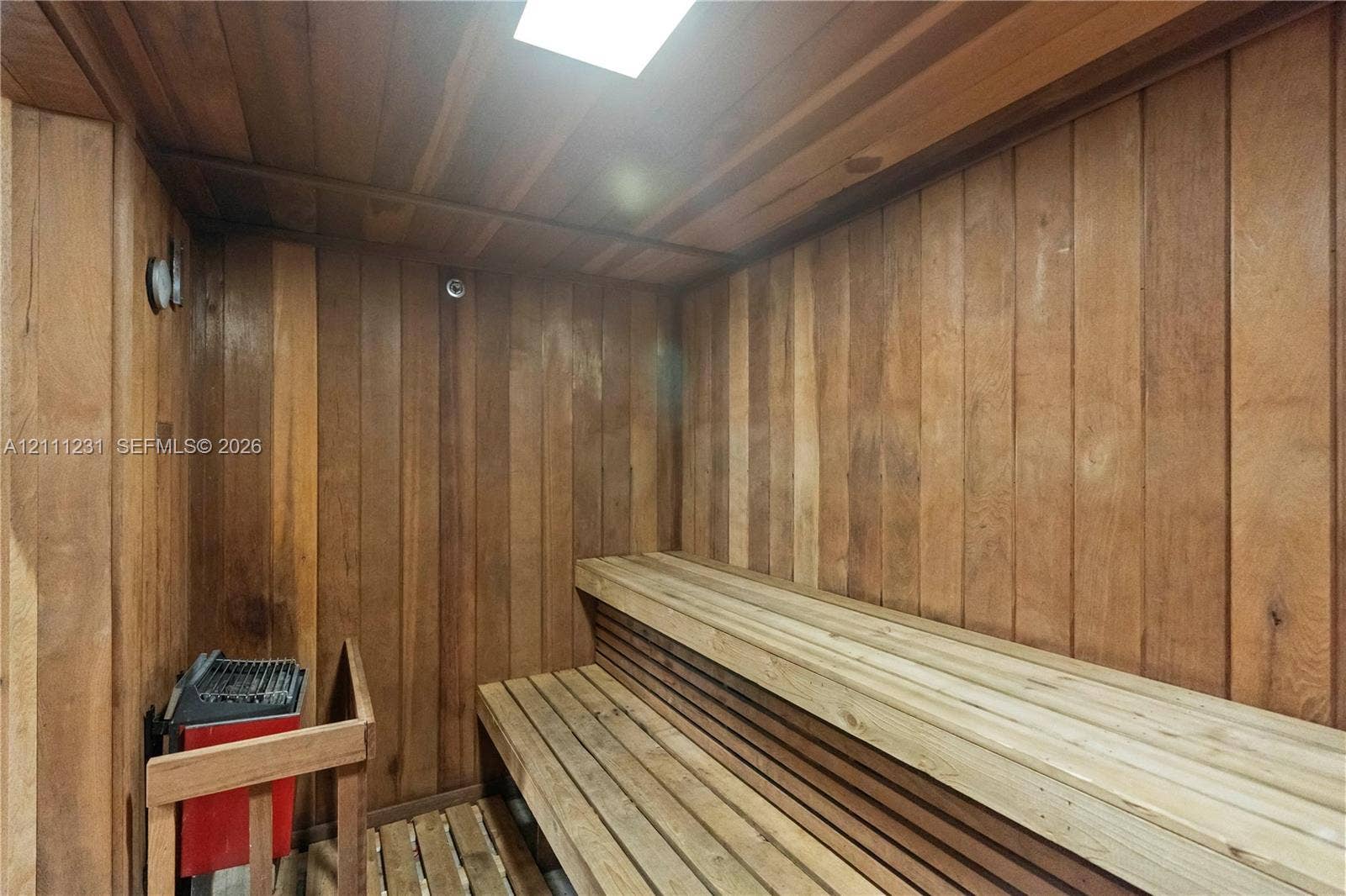 Sauna featuring vertical wood wall paneling, tiered slatted wood benches, and a built-in heating unit with a protective wood guard