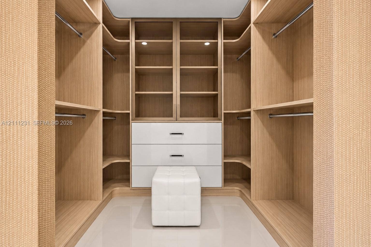 Custom closet featuring built-in wood-finish cabinetry, floor-to-ceiling shelving, integrated garment rods, and a white lacquer three-drawer storage unit