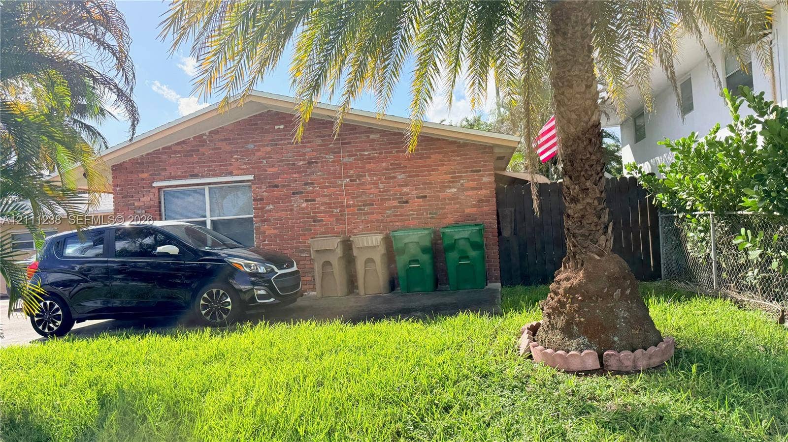 6100 SW 37th Street, Davie, FL 33314 Exterior featuring a brick facade, concrete driveway, and mature palm tree with stone-style landscape edging