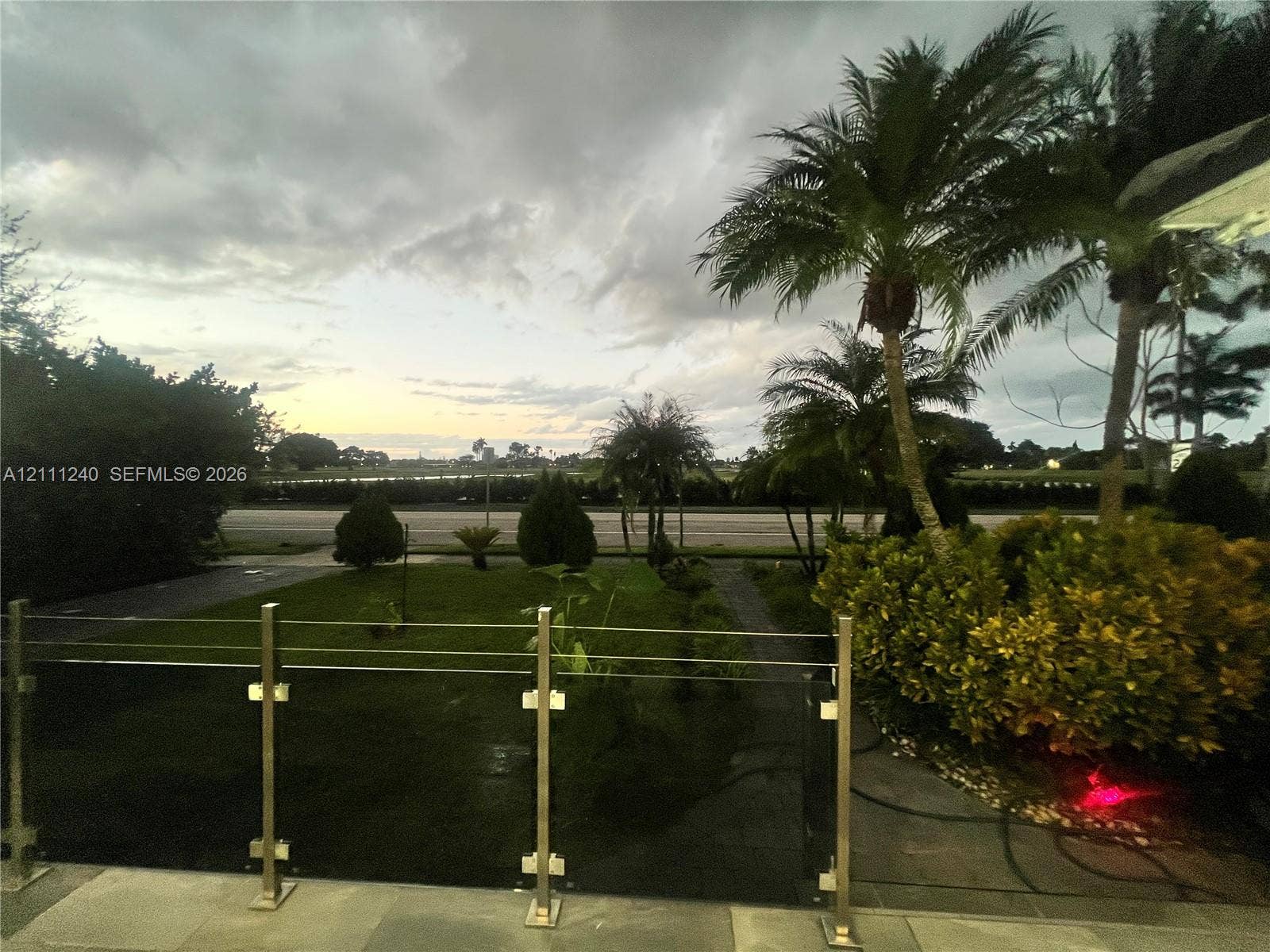 1430 Polk Street, Hollywood, Hollywood, FL 33020 Elevated outdoor terrace featuring a stainless steel and cable railing system, stone flooring, mature palm trees, manicured landscaping, and expansive open-air horizon scenery